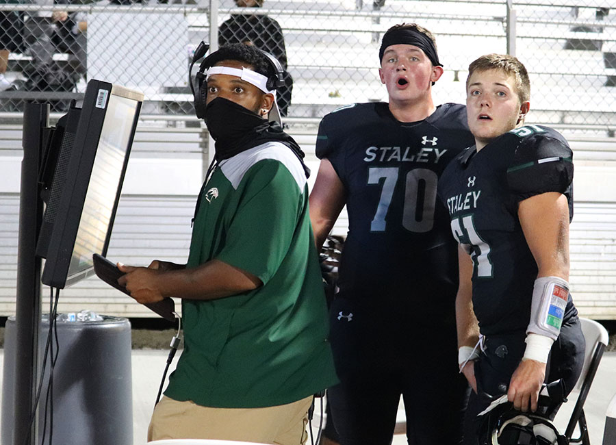 On the sidelines, juniors Zachary Sherwood, Anderson Hendershot and assistant coach Jared Simmons watch the play Oct. 9. Varsity defense made an important play and stop the opponents from making a first down, and they won 45-6 against Oak Park High School. “I felt excited and a bit worried that it wasn’t going to go right, but after the play I was extremely excited because our defense made the stop,” said Sherwood. Photo by Emma Thom