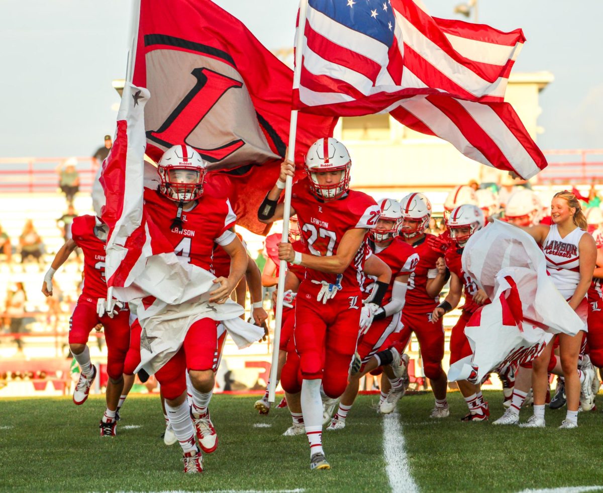 Continuing the tradition, senior Blaize Vaughn and sophomore Dawson Smith carry the flags as they tear through the banner with the rest of their varsity football team. "I am most excited to finally make a name for ourselves this season," Vaughn said. "It is no secret that we've struggled the last few years, but we are now a new team, a new brotherhood, and a new family." This game against Warsaw on Aug. 30 was the Cardinal's first of the season.